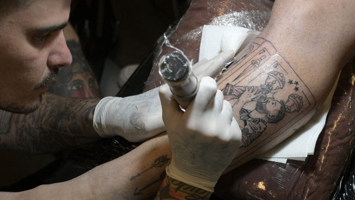 Argentine tattooist Tebi Cobra Vucinovich works on a tattoo of Argentina's forward Lionel Messi kissing the FIFA World Cup trophy on the leg of Ariel Sacchi at Ds Tattoo Shop in Buenos Aires on December 23, 2022. 