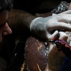 El tatuador argentino Tebi Cobra Vucinovich trabaja en un tatuaje de Lionel Messi besando el trofeo de la Copa Mundial de la FIFA en la pierna de Ariel Sacchi en Ds Tattoo Shop en Buenos Aires. | Foto:JUAN MABROMATA / AFP