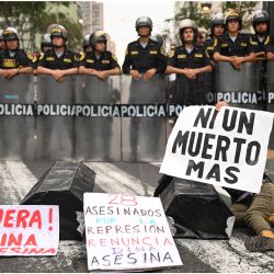 Ataúdes de cartón y un cartel que dice "28 asesinatos por la represión, dimisión Dina la asesina" se ven junto a miembros de la policía durante una manifestación contra el gobierno de la presidenta peruana Dina Boluarte en Lima. | Foto:ERNESTO BENAVIDES / AFP