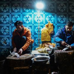 Personas preparan pescado en su tienda de un mercado mayorista de pescado de Rawalpindi, Pakistán. - El bullicioso mercado de pescado de Rawalpindi es más activo en invierno, de diciembre a marzo, cuando llegan unas 60 toneladas de marisco al día. | Foto:Farooq Naeem / AFP