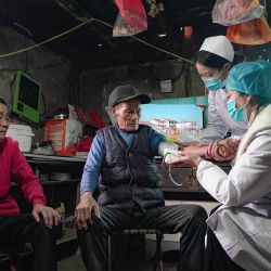 Esta foto muestra a un residente recibiendo un chequeo médico en el condado de Danzhai, prefectura autónoma de Qiandongnan Miao y Dong, en la provincia suroccidental china de Guizhou, mientras trabajadores médicos ofrecen chequeos médicos y botiquines para las personas que no pueden salir fácilmente de sus casas. | Foto:AFP