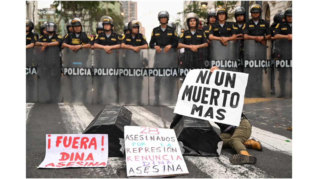 Ataúdes de cartón y un cartel que dice "28 asesinatos por la represión, dimisión Dina la asesina" se ven junto a miembros de la policía durante una manifestación contra el gobierno de la presidenta peruana Dina Boluarte en Lima. | Foto:ERNESTO BENAVIDES / AFP