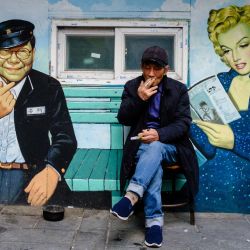 Un hombre fuma un cigarrillo sentado frente a un mural que representa a la presentadora de televisión surcoreana Song Hae y a la actriz estadounidense Marilyn Monroe a la salida de un cine en Seúl, Corea del Sur. | Foto:ANTHONY WALLACE / AFP