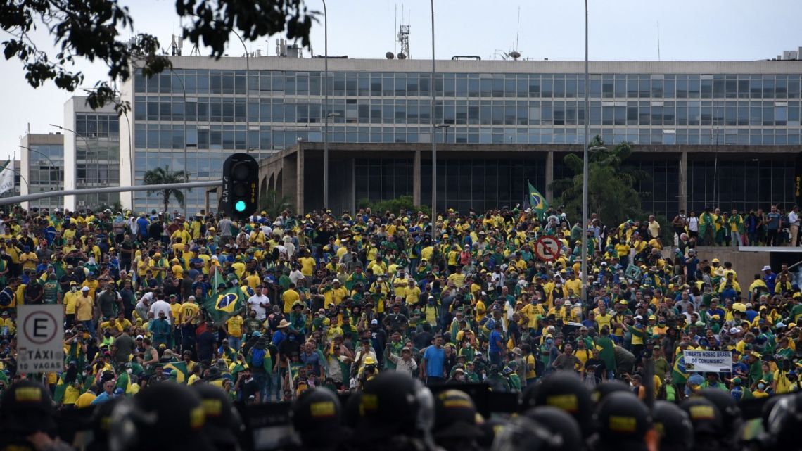 Supporters of Brazilian former President Jair Bolsonaro invading several governmental building are confronted by security forces (foreground) in Brasilia on January 8, 2023. Hundreds of supporters of Brazil's far-right ex-president Jair Bolsonaro broke through police barricades and stormed into Congress, the presidential palace and the Supreme Court Sunday, in a dramatic protest against President Luiz Inácio Lula da Silva's inauguration last week.