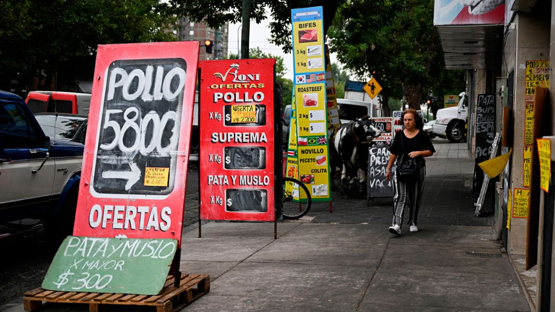 A woman walks between signs with food prices in the street in Buenos Aires on January 12, 2023.