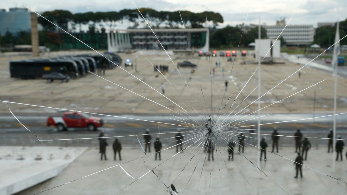 Security guards are seen through a broken window standing in front of the Planalto Palace during the inauguration of the new Minister of Indigenous Peoples, Sonia Guajajara, in Brasilia on January 11, 2023. Security was boosted in Brasilia Wednesday amid simmering tensions ahead of fresh protests by backers of ex-president Jair Bolsonaro and the pending arrest of one of his allies just days after riots shocked the Brazilian capital. 