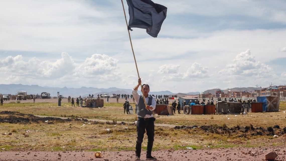A man waves a flag in front of police during a protest in a field adjacent to the airport in the Andean city of Juliaca, southern Peru, 11 January 2023. 