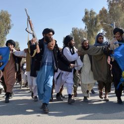 Un agente de seguridad talibán armado camina junto a unos hombres que protestan contra la quema del Corán por parte del político de extrema derecha sueco-danés Rasmus Paludan, en Kandahar. | Foto:Sanaullah Seiam / AFP