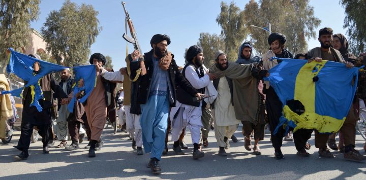 Un agente de seguridad talibán armado camina junto a unos hombres que protestan contra la quema del Corán por parte del político de extrema derecha sueco-danés Rasmus Paludan, en Kandahar.