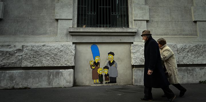Un grupo de personas pasa junto a un mural del artista callejero italiano AleXsandro Palombo titulado "Track 21 Los Simpson deportados a Auschwitz" cerca de la estación central de tren de Milán, con motivo del próximo Día Internacional de Conmemoración del Holocausto.