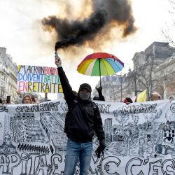 Un manifestante sostiene una bomba de humo delante de una pancarta anticapitalista durante una manifestación en un segundo día de huelgas y protestas en todo el país por la reforma de las pensiones propuesta por el gobierno, en París, Francia. | Foto:JULIEN DE ROSA / AFP