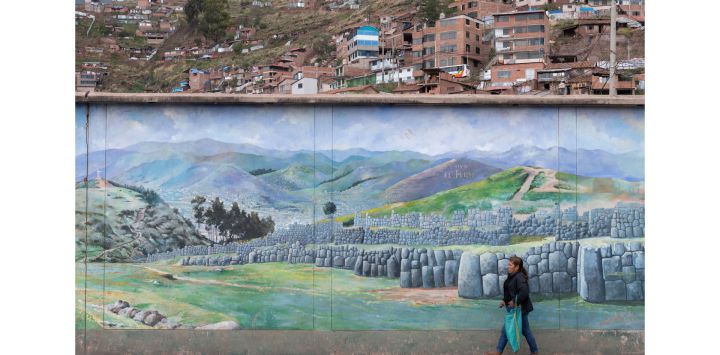 Una mujer camina junto a un mural de la fortaleza inca de Sacsahuaman en la ciudad de Cusco, Perú,, mientras el número de turistas que llegan al popular destino turístico sigue disminuyendo debido a las protestas en curso en todo el país.