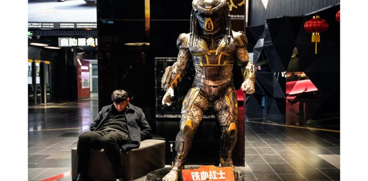 Un hombre duerme junto a una estatua a tamaño real del personaje cinematográfico Predador en un centro comercial de Pekín.