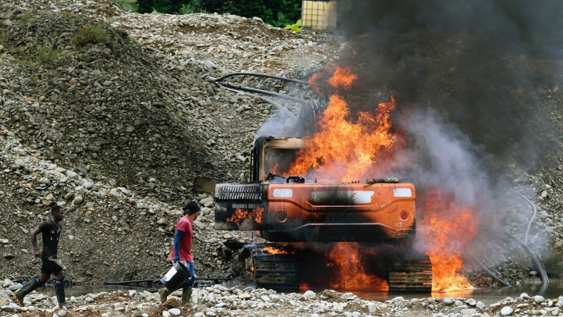 Locals try to extinguish the fire on heavy machinery, destroyed by armed forces during an operation at an illegal gold mining place in Triangulo de Telembi, Colombia on January 25, 2023. 