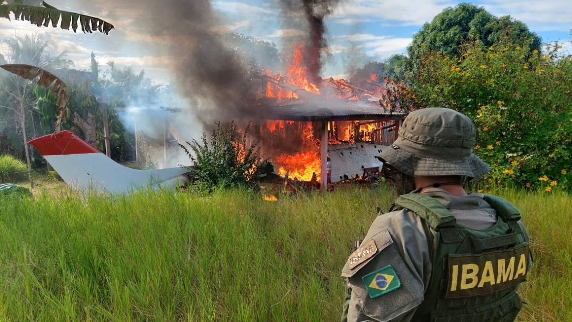 Handout picture released by the Brazilian Institute of Environment and Renewable Natural Resources (IBAMA) showing a member of the environmental agency looking at an aircraft belonging to illegal miners being consumed by fire during an operation against Amazon deforestation, at the Yanomami territory in Roraima State, Brazil, on February 6, 2023. 