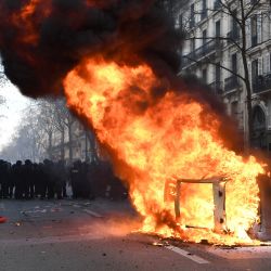 Policías antidisturbios franceses permanecen detrás de un coche en llamas al margen de una manifestación en el cuarto día de concentraciones organizadas en todo el país desde principios de año, contra una revisión de las pensiones profundamente impopular, en París. | Foto:BERTRAND GUAY / AFP