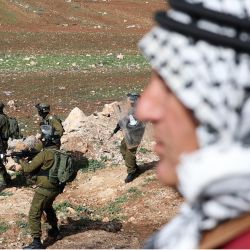 Soldados israelíes toman posiciones mientras un palestino mira durante los enfrentamientos tras una protesta contra el establecimiento de puestos de avanzada israelíes, en Beit Dajan, al este de la ciudad ocupada de Naplusa, en Cisjordania. | Foto:JAAFAR ASHTIYEH / AFP