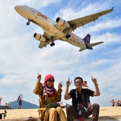 En esta imagen unos turistas posan para una foto en la playa de Mai Khao mientras un avión aterriza en el aeropuerto internacional de Phuket, en la provincia de Phuket, Tailandia. | Foto:MADAREE TOHLALA / AFP