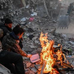 Residentes locales queman libros para mantenerse calientes mientras esperan a que sus familiares sean sacados de entre los escombros de los edificios derrumbados en Hatay, Turquía, después de que un terremoto de magnitud 7,8 sacudiera el sureste del país. | Foto:BULENT KILIC / AFP