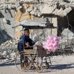Un niño sirio que vende algodón de azúcar sonríe frente a los escombros de un edificio derrumbado tras el terremoto de la semana pasada en la localidad rebelde siria de Atarib. | Foto:AAREF WATAD / AFP