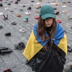 La diseñadora ucraniana Margarita Chala, ataviada con una bandera ucraniana, junto a los zapatos que simbolizan los crímenes de guerra cometidos contra civiles ucranianos en la Plaza de la Ciudad Vieja de Praga (República Checa) con motivo del primer aniversario de la invasión rusa de Ucrania. | Foto:Michal Cizek / AFP