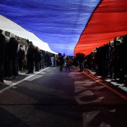 Manifestantes sostienen una bandera serbia gigante durante una concentración contra las autoridades serbias y el plan franco-alemán para la resolución de Kosovo, en Belgrado, Serbia. | Foto:OLIVER BUNIC / AFP