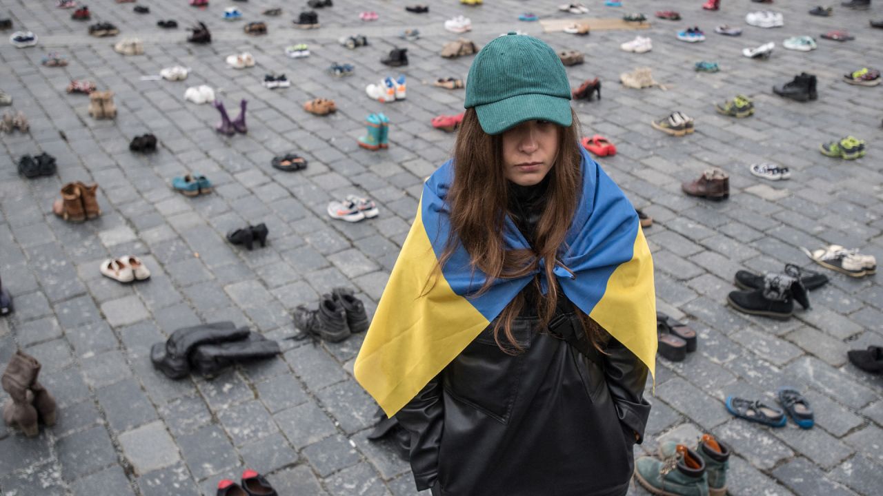 La diseñadora ucraniana Margarita Chala, ataviada con una bandera ucraniana, junto a los zapatos que simbolizan los crímenes de guerra cometidos contra civiles ucranianos en la Plaza de la Ciudad Vieja de Praga (República Checa) con motivo del primer aniversario de la invasión rusa de Ucrania. | Foto:Michal Cizek / AFP