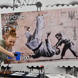 Una mujer saca una foto de sellos y sobres en la principal oficina de correos durante la presentación de un nuevo sello ucraniano con un dibujo de Banksy, en Kiev. | Foto:SERGEI SUPINSKY / AFP