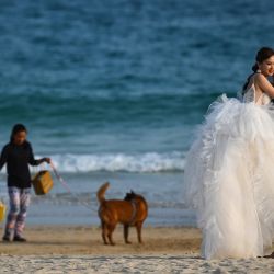 Una pareja posa para sus fotos de boda mientras la gente pasea a su perro en una playa de Hong Kong. | Foto:PETER PARKS / AFP
