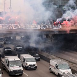 Los conductores de autobús de la empresa estatal RATP, que gestiona el sistema de transporte metropolitano de París, queman bengalas detrás de una pancarta en un puente sobre la carretera de circunvalación de París  | Foto:THOMAS SAMSON / AFP