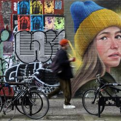 Un peatón pasa junto a un grafiti de arte callejero que representa a una mujer con un sombrero con los colores de la bandera nacional de Ucrania, obra de Woskerski art, en Londres. | Foto:ISABEL INFANTES / AFP