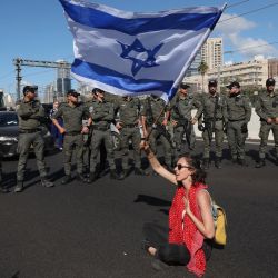 Fuerzas israelíes montan guardia mientras un manifestante ondea una bandera nacional durante una manifestación contra el controvertido proyecto de reforma judicial del gobierno en Tel Aviv. | Foto:JACK GUEZ / AFP