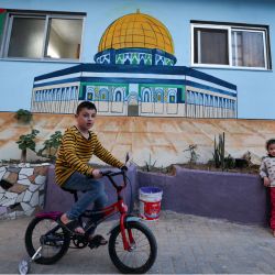 Un niño en una bicicleta delante de un muro, pintado con vivos colores como parte de una iniciativa de un artista palestino, en el distrito de Zeitun de la ciudad de Gaza. | Foto:MAHMUD HAMS / AFP