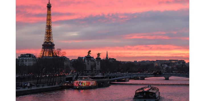 La foto muestra al puente Alejandro III y la Torre Eiffel mientras el barco turístico bateau mouche navega por el río Sena al atardecer en París.