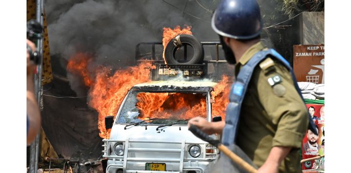 Un policía junto a un vehículo en llamas durante los enfrentamientos entre partidarios del ex primer ministro Imran Khan y la policía antidisturbios cerca de la casa de Khan para impedir que los agentes lo detuvieran, en Lahore, Pakistán.