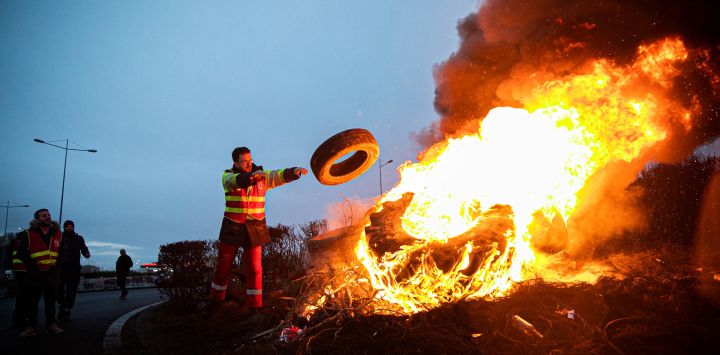 Una persona alimenta un fuego en una carretera, cerca de una gasolinera de TotalEnergies, en Le Havre, noroeste de Francia, mientras bloquean la zona industrial.