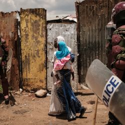 Una mujer con una niña en brazos camina mientras agentes de policía bloquean la calle durante una manifestación convocada por el líder de la oposición Raila Odinga, que afirma que le robaron las últimas elecciones presidenciales de Kenia y culpa al gobierno de la subida del costo de la vida, en Kibera, Nairobi. | Foto:YASUYOSHI CHIBA / AFP