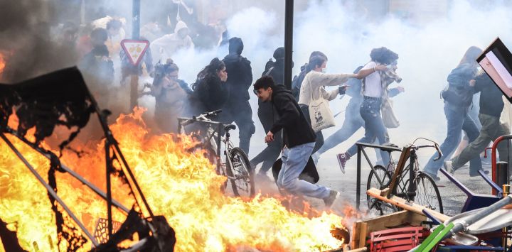 Manifestantes corren entre el humo de gases lacrimógenos junto a una hoguera callejera durante una manifestación en el marco de una jornada nacional de huelgas y protestas, una semana después de que el gobierno francés impulsara una reforma de las pensiones en el Parlamento sin someterla a votación, amparándose en el artículo 49.3 de la Constitución, en Toulouse, sur de Francia.