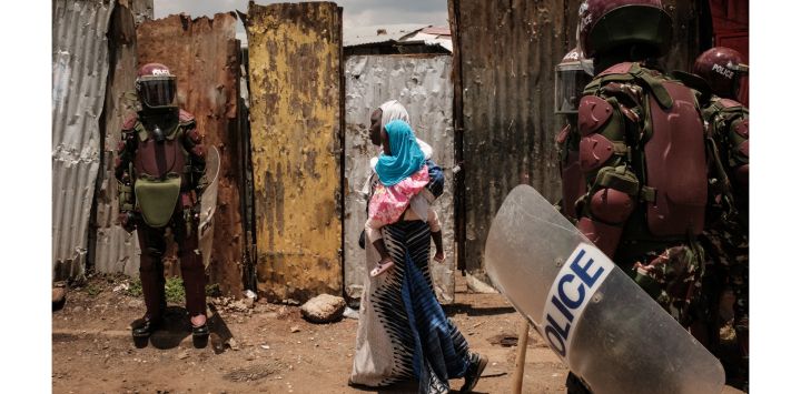 Una mujer con una niña en brazos camina mientras agentes de policía bloquean la calle durante una manifestación convocada por el líder de la oposición Raila Odinga, que afirma que le robaron las últimas elecciones presidenciales de Kenia y culpa al gobierno de la subida del costo de la vida, en Kibera, Nairobi.