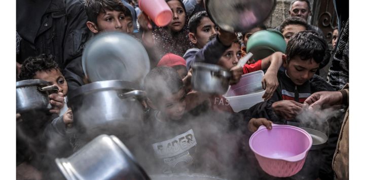 Unos jóvenes extienden sus ollas y recipientes para recibir sopa preparada por el palestino Walid al-Hattab, mientras rompen el ayuno en el segundo día del mes sagrado musulmán del Ramadán en la ciudad de Gaza.