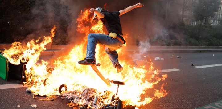 Un manifestante pasa con un monopatín por encima de contenedores de basura en llamas durante una manifestación después de que el gobierno impulsara una reforma de las pensiones a través del parlamento sin votación, utilizando el artículo 49.3 de la Constitución, en Toulouse, sur de Francia.