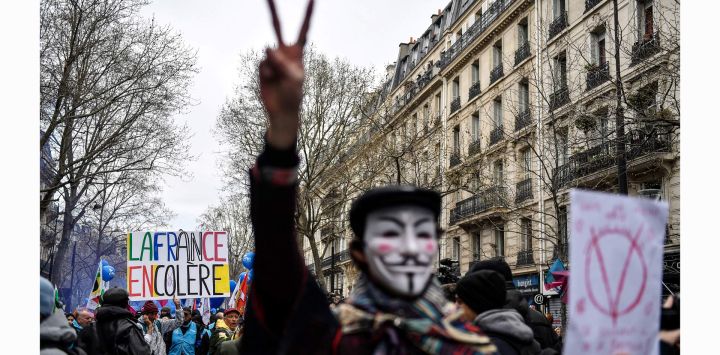Un manifestante sostiene una pancarta en la que se lee "Francia en cólera" mientras otro con una máscara de Guy Fawkes hace el gesto de la V durante una manifestación después de que el gobierno impulsara una reforma de las pensiones a través del parlamento sin votación, utilizando el artículo 49.3 de la Constitución, en París.