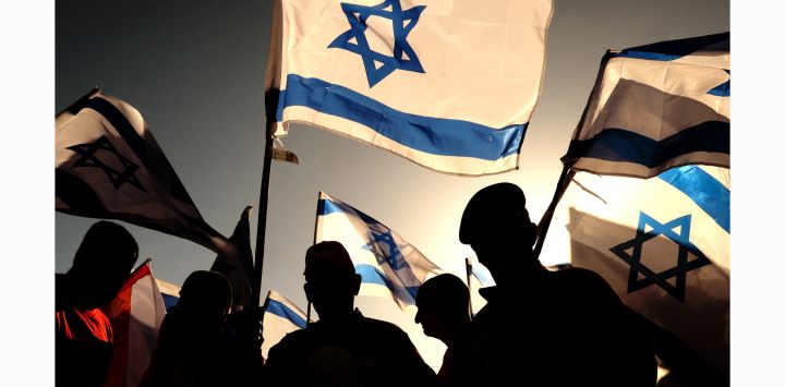 Veteranos militares israelíes ondean banderas nacionales durante una manifestación contra el proyecto de reforma judicial del gobierno, a lo largo de una carretera cerca de Netanya.