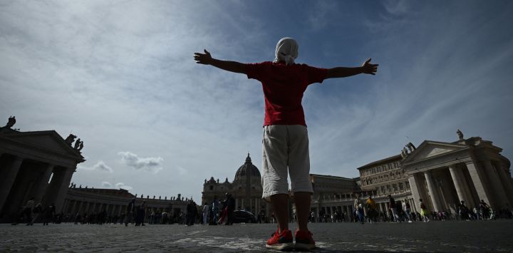 Un hombre permanece con los brazos abiertos hacia la basílica de San Pedro en El Vaticano, un día después de que el Papa fuera ingresado en el hospital Gemelli de Roma.