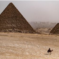 En esta imagen un guía de camellos cabalga cerca de la Pirámide de Menkaure en la necrópolis de las Pirámides de Guiza, a las afueras de la capital egipcia. | Foto:AMIR MAKAR / AFP