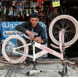 Un reparador de bicicletas trabaja en una bicicleta en su tienda de la ciudad de Gaza. | Foto:MOHAMMED ABED / AFP