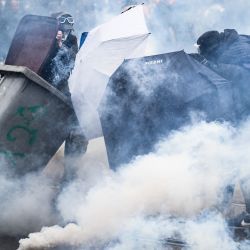 Manifestantes se protegen del humo de gases lacrimógenos detrás de paraguas y contenedores de basura durante los enfrentamientos durante una manifestación en el undécimo día de acción después de que el gobierno impulsara una reforma de las pensiones a través del parlamento sin votación, utilizando el artículo 49.3 de la constitución, en Nantes, oeste de Francia. | Foto:LOIC VENANCE / AFP