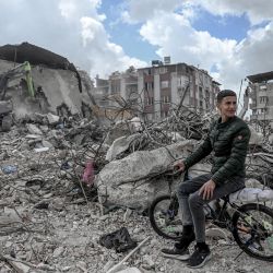 Un joven en bicicleta busca sus pertenencias mientras se retiran los escombros de su casa, dos meses después de que un terremoto arrasara franjas del montañoso sureste de Turquía, en Antakya. | Foto:OZAN KOSE / AFP