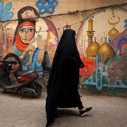 Una mujer pasa junto a la representación de mujeres abrazándose y un santuario musulmán, en un mural artístico en la pared de una casa del barrio de al-Anbari de Bagdad, Irak. | Foto:AHMAD AL-RUBAYE / AFP