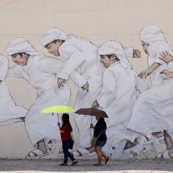 Unas mujeres pasan junto a un mural de niños emiratíes en uno de los mercados de Dubai. | Foto:KARIM SAHIB / AFP